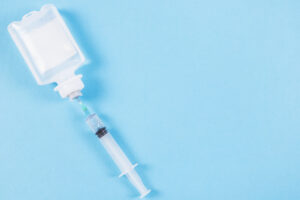 Syringe inserted into IV pouch on a blue background